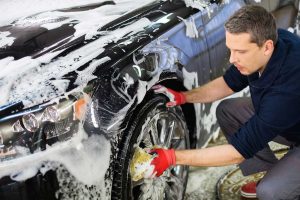 Care detailer cleans a wheel and tire with soap and sponge