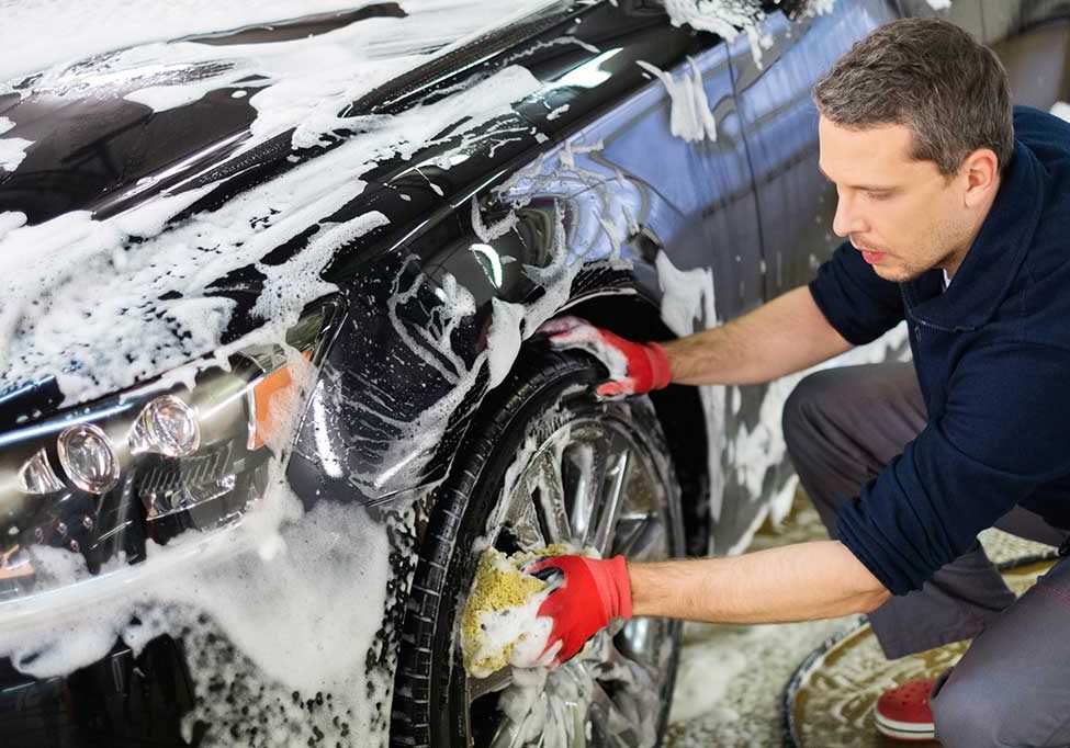 Care detailer cleans a wheel and tire with soap and sponge